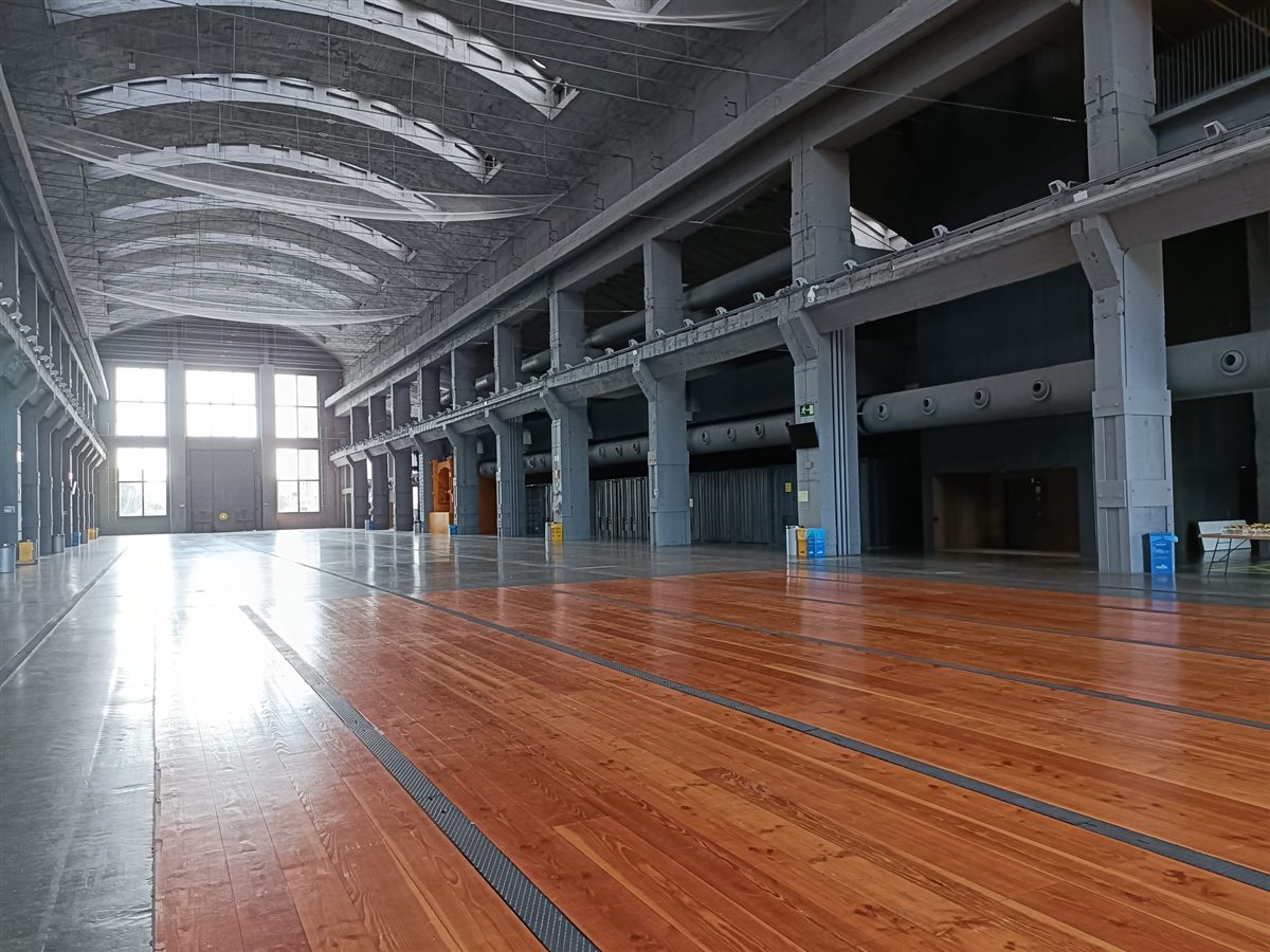 A large empty hall with a wooden floor and rows of columns. Velika prazna hala s drvenim podom i redovima stupova.