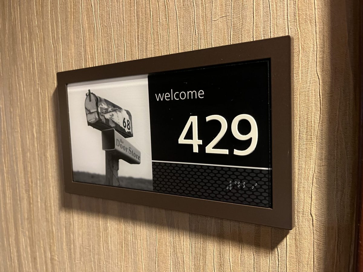 A hotel room door sign with the room number printed and in braille. A hotel room door sign with the room number printed and in braille.