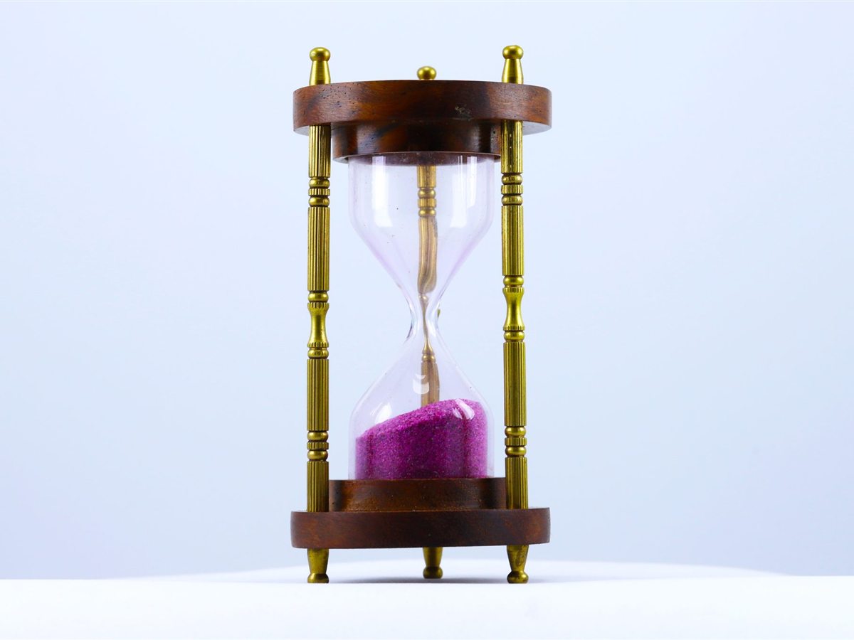 An hourglass with a wooden frame and pink sand on a white background. An hourglass with a wooden frame and pink sand on a white background.