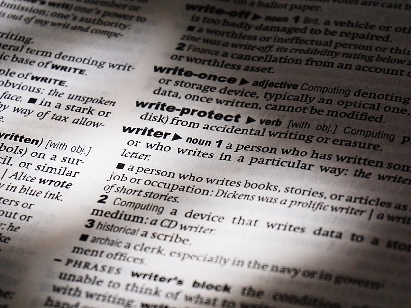 Close-up of a dictionary page with entries around the word write Dvije ispisane verzije istog dokumenta na različitim jezicima leže jedna uz drugu na stolu, a olovka označava razlike.