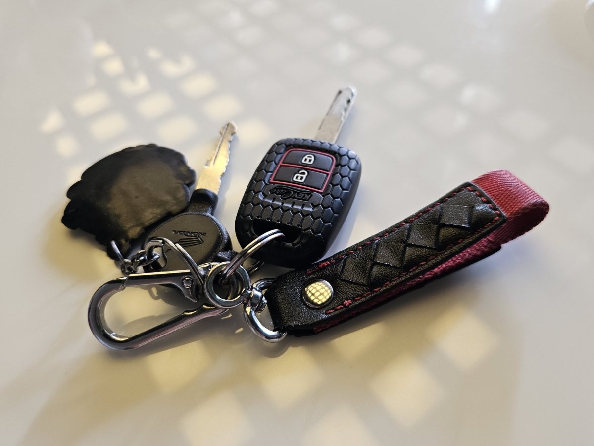 A bunch of keys with a car key and a leather strap lying on a white table Jedna osoba predaje drugoj svežanj ključeva preko uredskog stola.